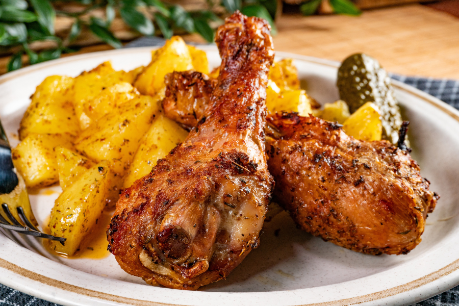 Roasted pasture raised chicken drumsticks with potatoes on a white plate