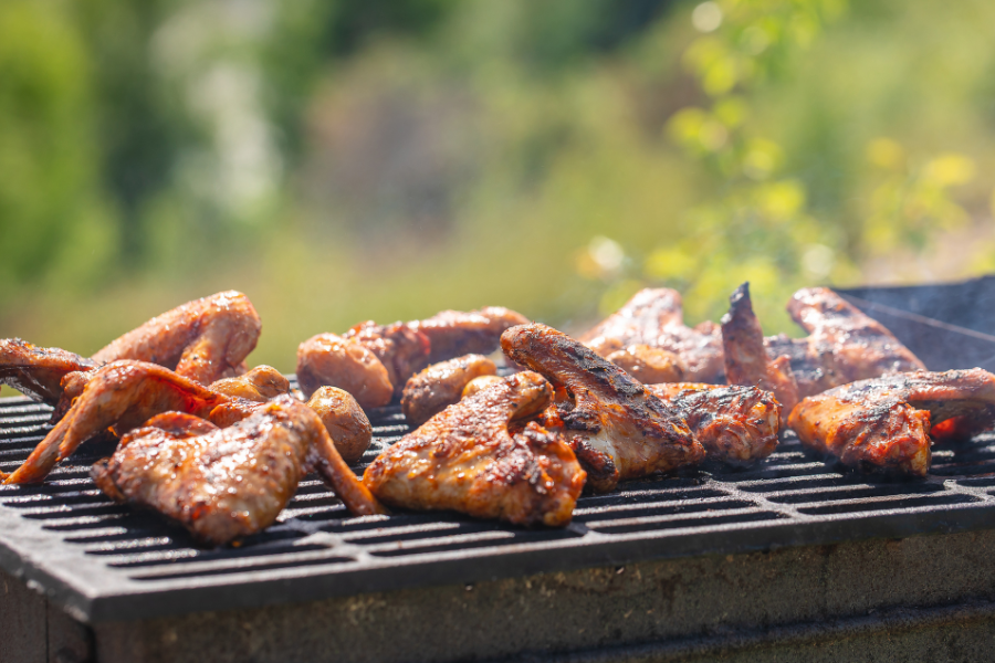 Grilled pasture-raised chicken wings on a barbecue grill with a blurred green background