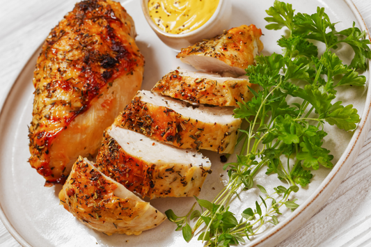 Sliced roasted non-GMO pasture-raised bone in chicken breast on a plate with herbs and mustard.