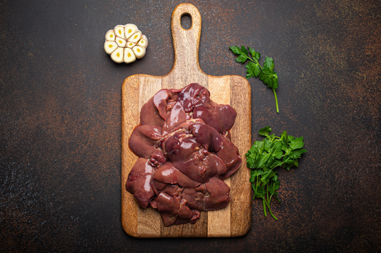 Raw local pasture raised duck and chicken livers on a wooden cutting board with herbs on a dark surface