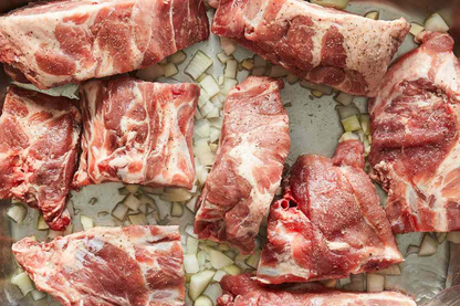 Raw local farm pasture raised pork bones pieces on a baking tray with onions
