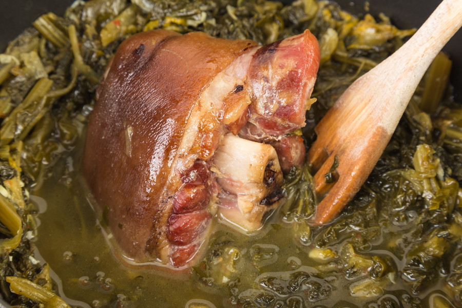 Local pasture raised pork knuckle ham hocks with greens in a pan with a wooden spoon