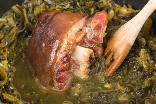 Local pasture raised pork knuckle ham hocks with greens in a pan with a wooden spoon