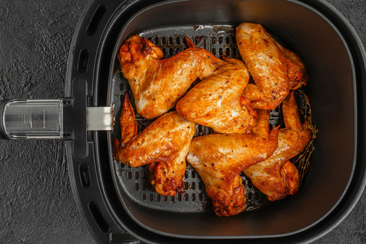 Air fryer basket with crispy pasture raised chicken wings, antibiotic free, on a dark background