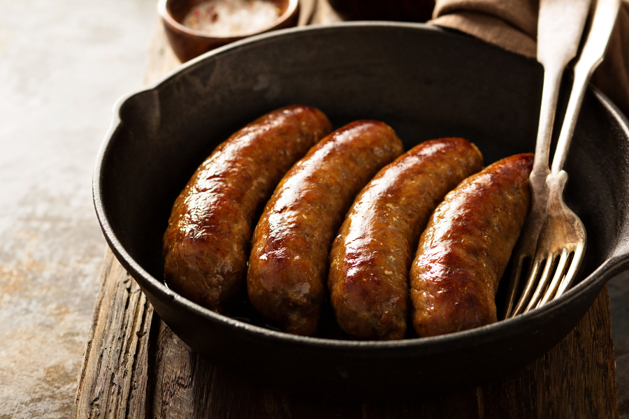 Four forest raised pork sausages in a black cast iron skillet show a sample cut from our meat CSA subscription