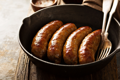 Four forest raised pork sausages in a black cast iron skillet show a sample cut from our meat CSA subscription
