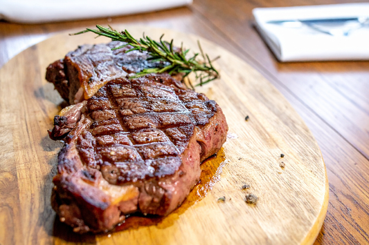 Grilled local grassfed ribeye steak on a wooden cutting board with rosemary, on a wooden table.