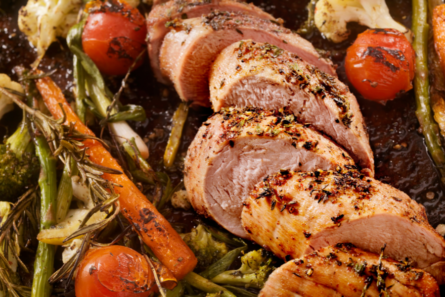 Sliced roasted local farm pork tenderloin with vegetables on a baking tray