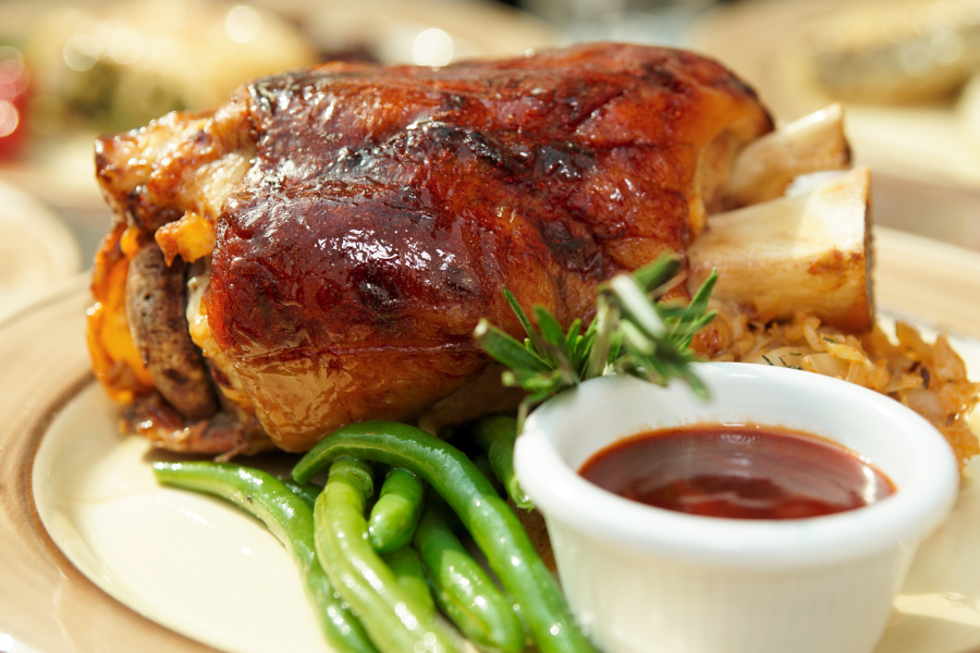 Roasted local NC farm pasture raised pork shanks with green beans and a side of sauce on a plate.