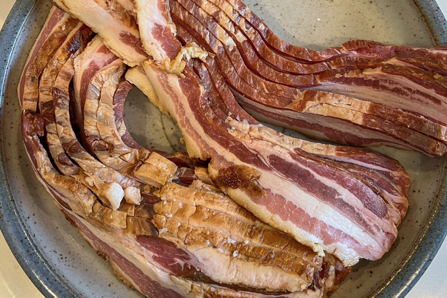 Sliced forest raised bacon from Carolina Pastures bacon on a ceramic plate