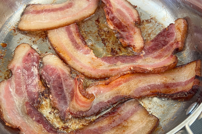 Pasture raised bacon from Carolina Pastures cooking in a skillet with local pork delivery in Raleigh