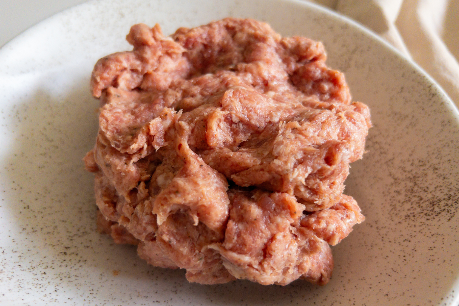 Raw non-GMO forest raised pork sausage on a speckled ceramic plate with local pork delivery