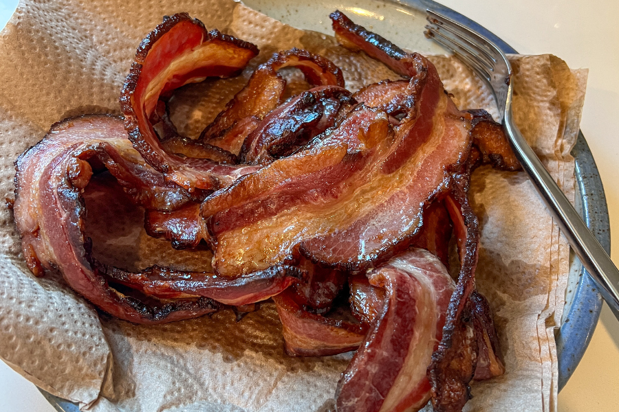 local pastured bacon strips on a paper towel with a fork on a plate