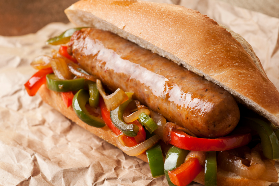 local pasture pork italian sausage with peppers and onions on a bun on a paper wrapper