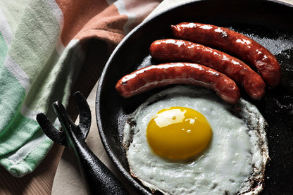 Cooked local farm pastured pork maple breakfast sausages in a skillet with a fried egg
