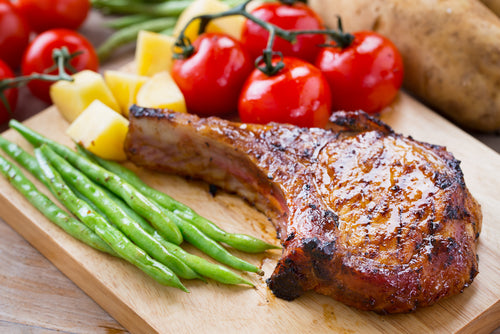 Baked non-GMO forest-raised pork chop from carolina pastures on a cutting board with vegetables