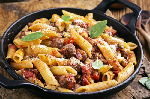 A pan of pasta with forest raised pork bulk italian sausage, tomatoes, and herbs, garnished with cheese and basil leaves.